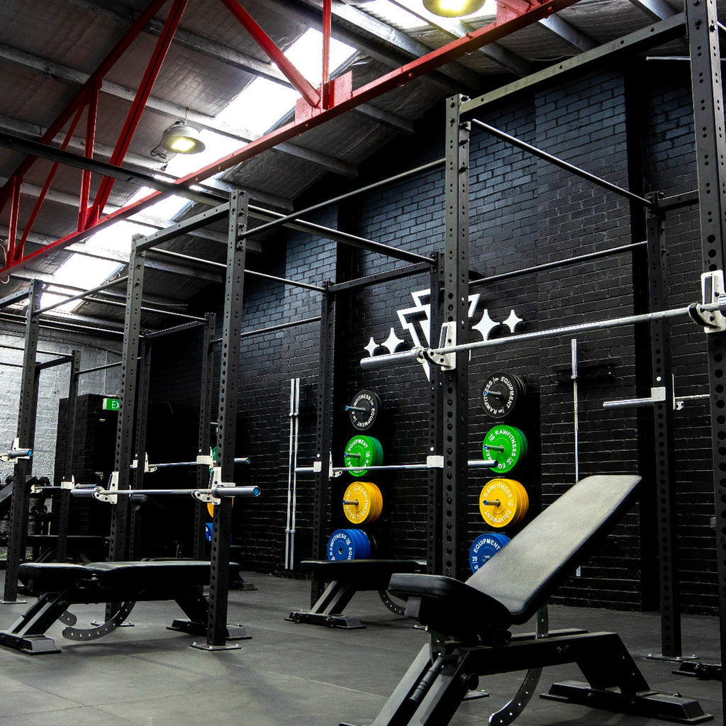 Gym interior with weightlifting equipment against a black brick wall.